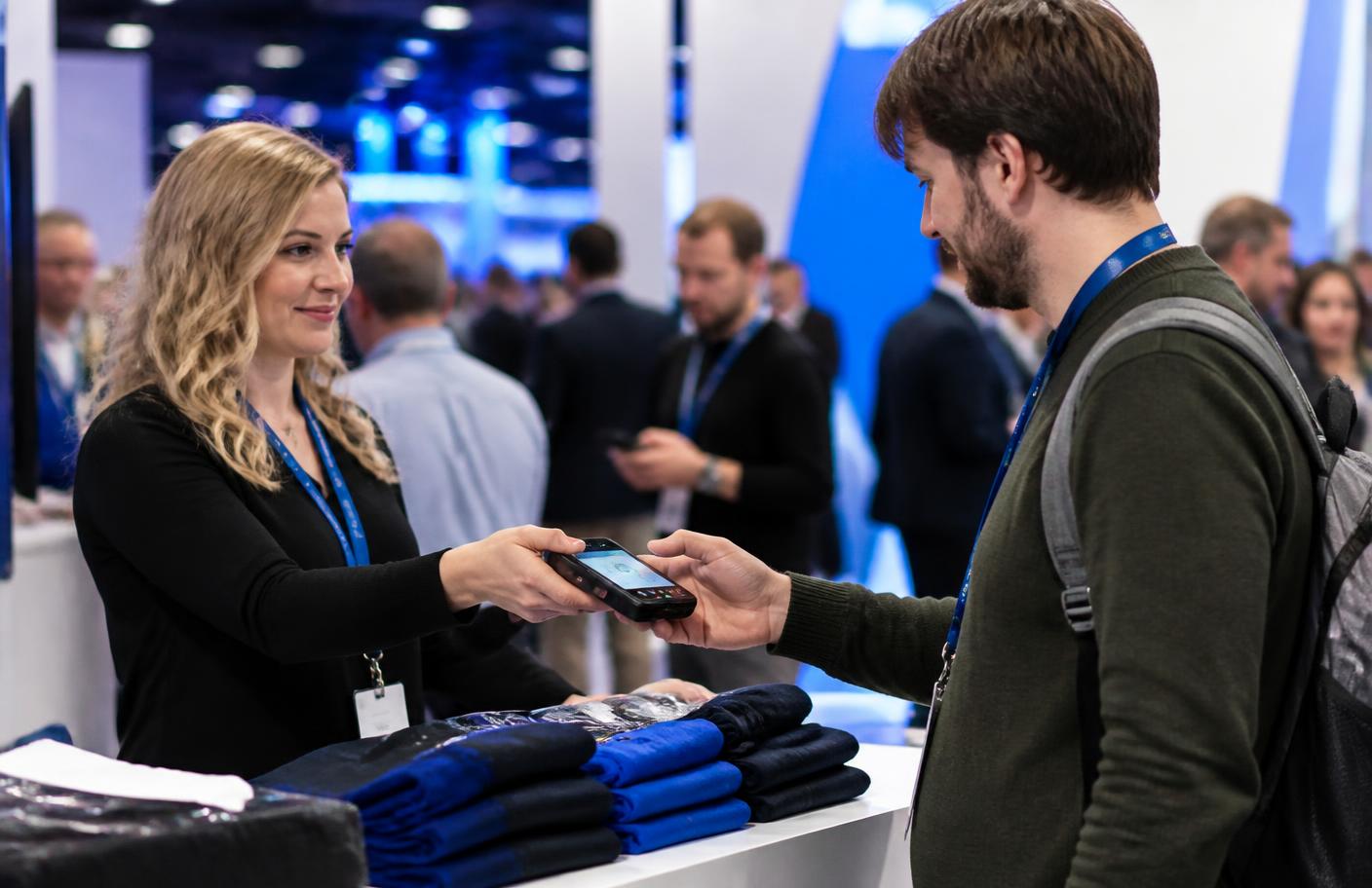 Conference expo booth staff taking a contactless payment from an attendee on a handheld terminal